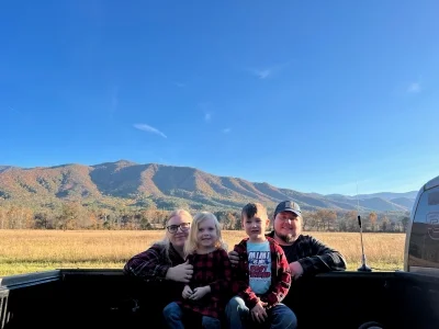 Family photo of family sitting on bed of a truck with mountains in the background. Dedicated web-designer.
